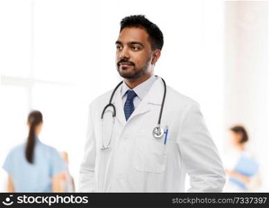 medicine, profession and healthcare concept - indian male doctor in white coat with stethoscope over hospital background. indian male doctor with stethoscope