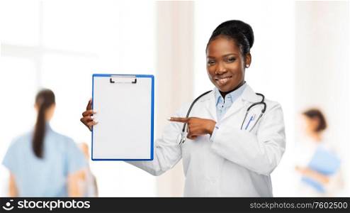medicine, profession and healthcare concept - smiling african american female doctor in white coat with clipboard and stethoscope over hospital staff on background. african american female doctor with clipboard