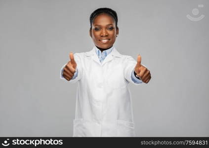 medicine, profession and healthcare concept - smiling african american female doctor or scientist in white coat showing thumbs up over grey background. african american female doctor showing thumbs up