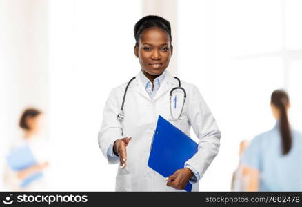 medicine, profession and healthcare concept - smiling african american female doctor or scientist in white coat with clipboard over hospital staff on background. happy african american female doctor or scientist