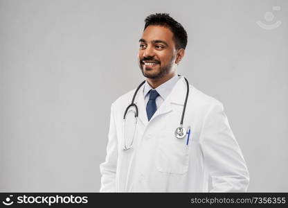 medicine, profession and healthcare concept - smiling indian male doctor in white coat with stethoscope over grey background. smiling indian male doctor with stethoscope