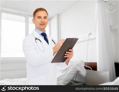 medicine, profession and healthcare concept - smiling male doctor with clipboard and stethoscope writing prescription over hospital ward background. smiling male doctor with clipboard and stethoscope