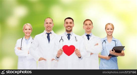 medicine, profession, teamwork and healthcare concept - group of smiling medics or doctors holding red paper heart shape, clipboard and stethoscopes over green background