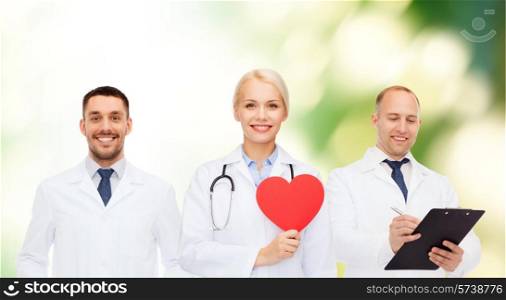 medicine, profession, teamwork and healthcare concept - group of smiling medics or doctors holding red paper heart shape, clipboard and stethoscopes over green background