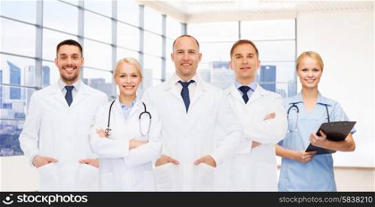 medicine, profession, teamwork and healthcare concept - group of smiling medics or doctors with clipboard and stethoscopes over clinic background