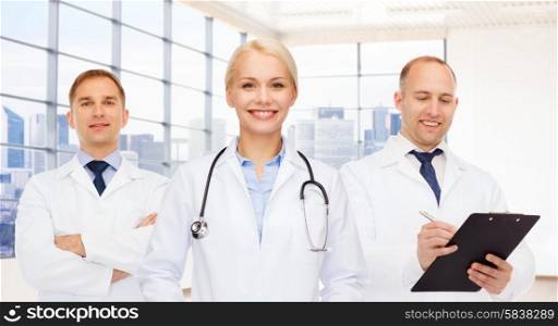 medicine, profession, teamwork and healthcare concept - group of smiling medics or doctors with clipboard and stethoscopes over clinic background