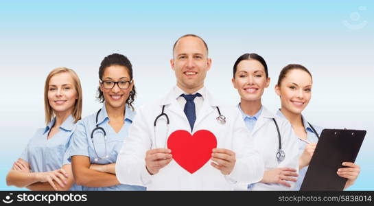 medicine, profession, teamwork and healthcare concept - international group of smiling medics or doctors with clipboard and stethoscopes holding red paper heart shape over blue background