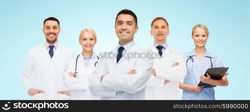 medicine, profession, teamwork and healthcare concept - international group of smiling medics or doctors with clipboard and stethoscopes over blue background