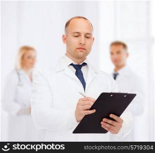 medicine, profession, teamwork and healthcare concept - serious male doctor with clipboard writing prescription over group of medics