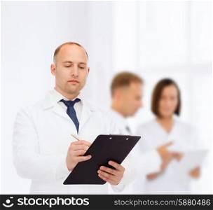 medicine, profession, teamwork and healthcare concept - serious male doctor with clipboard writing prescription over group of medics