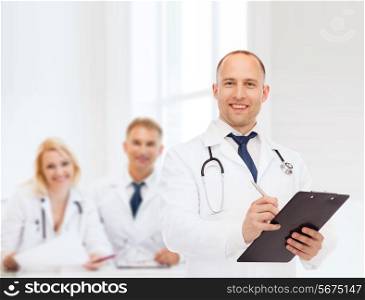 medicine, profession, teamwork and healthcare concept - smiling male doctor with clipboard and stethoscope writing prescription over group of medics