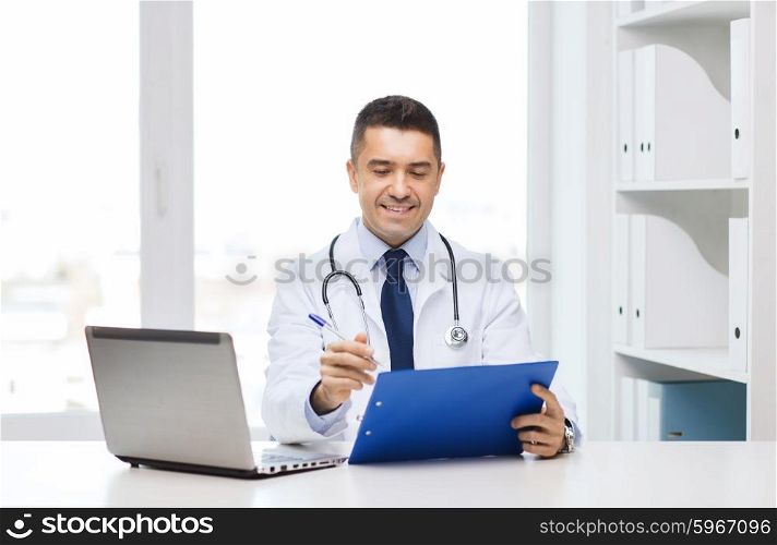 medicine, profession, technology and people concept - happy male doctor with clipboard and laptop computer in medical office