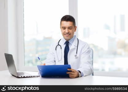 medicine, profession, technology and people concept - happy male doctor with clipboard and laptop computer in medical office