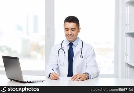 medicine, profession, technology and people concept - smiling male doctor with laptop in medical office