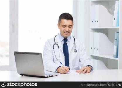 medicine, profession, technology and people concept - smiling male doctor with laptop in medical office