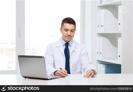 medicine, profession, technology and people concept - smiling male doctor with laptop in medical office