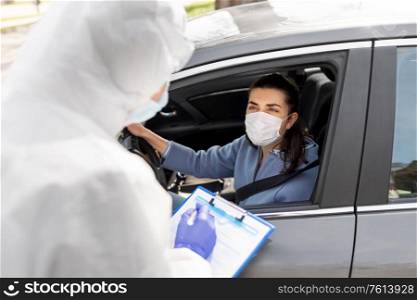 medicine, quarantine and pandemic concept - doctor or healthcare worker in protective gear or hazmat suit, medical mask, gloves and goggles and woman waiting for coronavirus test in her car. healthcare worker with clipboard and woman in car