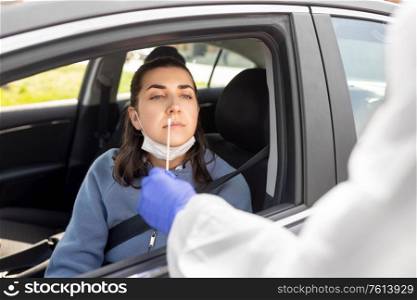 medicine, quarantine and pandemic concept - doctor or healthcare worker in protective gear or hazmat suit with cotton swab making coronavirus test for young woman in her car. healthcare worker making coronavirus test at car