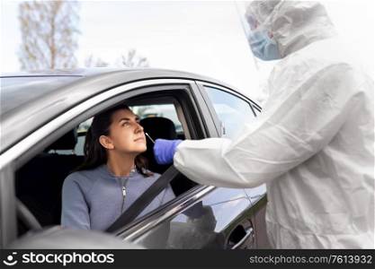 medicine, quarantine and pandemic concept - doctor or healthcare worker in protective gear or hazmat suit with beaker and cotton swab making coronavirus test for young woman in her car. healthcare worker making coronavirus test at car