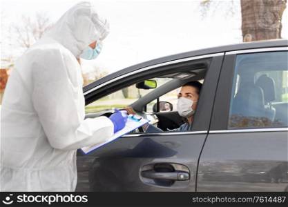 medicine, quarantine and pandemic concept - doctor or healthcare worker in protective gear, medical mask, gloves and goggles with clipboard and woman waiting for coronavirus test in her car. healthcare worker with clipboard and woman in car