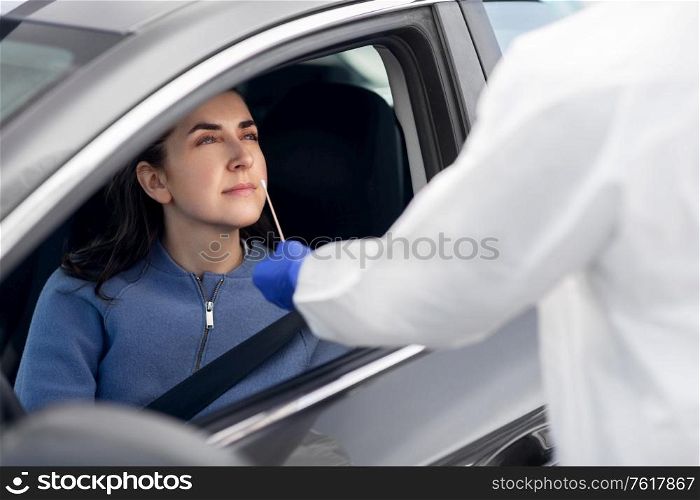 medicine, quarantine and pandemic concept - doctor or healthcare worker in protective gear or hazmat suit with cotton swab making coronavirus test for young woman in her car. healthcare worker making coronavirus test at car