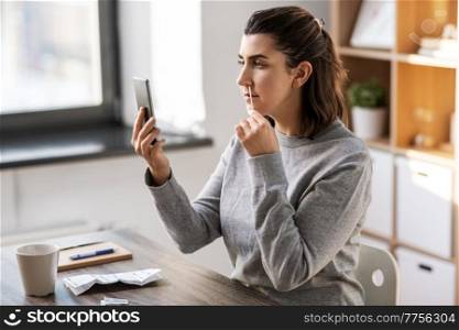 medicine, quarantine and pandemic concept - woman with swab and smartphone taking sample from her nose and making nasal coronavirus self test at home. woman making coronavirus self test at home