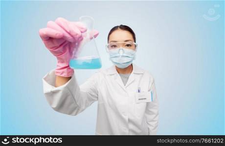 medicine, science and healthcare concept - asian female doctor or scientist wearing face protective medical mask and goggles holding flask with chemical or cure over blue background. asian doctor or scientist in mask with flask