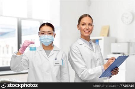 medicine, science and healthcare concept - happy smiling female doctors or scientists in white coats with clipboard and test tube over medical office at hospital on background. smiling female doctors or scientists at hospital
