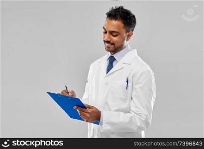 medicine, science and profession concept - smiling indian male doctor or scientist in white coat with clipboard over grey background. smiling indian doctor or scientist with clipboard