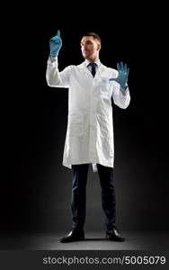 medicine, science, healthcare and people concept - doctor or scientist in white coat and medical gloves touching something invisible over black background. doctor or scientist in lab coat and medical gloves