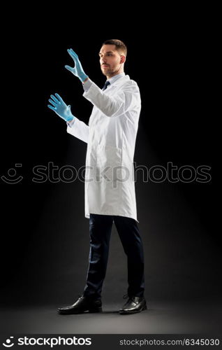 medicine, science, healthcare and people concept - doctor or scientist in white coat and medical gloves touching something invisible over black background. doctor or scientist in lab coat and medical gloves