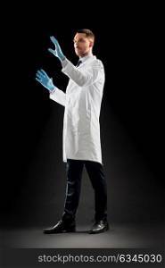 medicine, science, healthcare and people concept - doctor or scientist in white coat and medical gloves touching something invisible over black background. doctor or scientist in lab coat and medical gloves