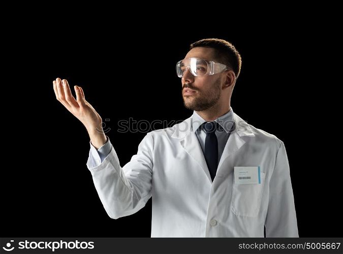 medicine, science, healthcare and people concept - male doctor or scientist in white coat and safety glasses touching something invisible over black background. doctor or scientist in lab coat and safety glasses