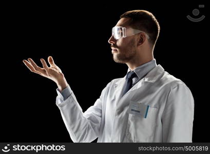 medicine, science, healthcare and people concept - male doctor or scientist in white coat and safety glasses touching something invisible over black background. doctor or scientist in lab coat and safety glasses