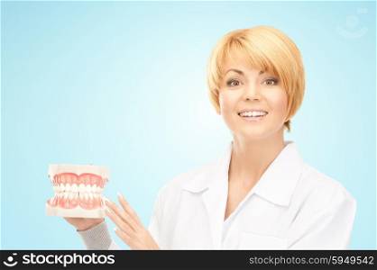 medicine, stomatology, people and dental hygiene concept - smiling female doctor with jaws model over blue background