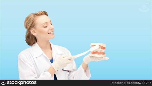 medicine, stomatology, people and hygiene concept - smiling female doctor with toothbrush and jaws model teaching how to brush teeth over blue background