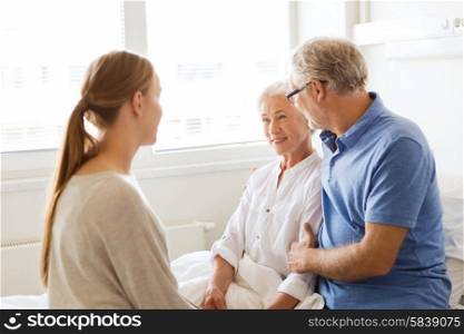 medicine, support, family health care and people concept - happy senior man and young woman visiting and cheering her grandmother lying in bed at hospital ward