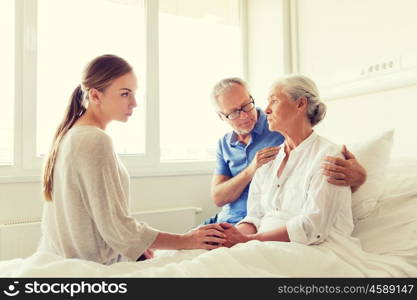 medicine, support, family health care and people concept - senior man and young woman visiting and cheering her ill grandmother at hospital ward