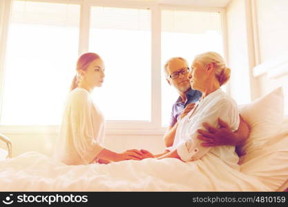 medicine, support, family health care and people concept - senior man and young woman visiting and cheering her ill grandmother at hospital ward