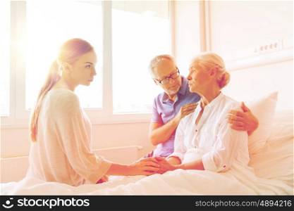 medicine, support, family health care and people concept - senior man and young woman visiting and cheering her ill grandmother at hospital ward