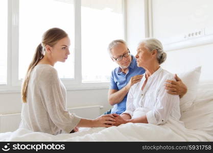 medicine, support, family health care and people concept - senior man and young woman visiting and cheering her ill grandmother at hospital ward