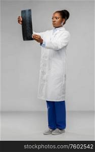 medicine, surgery and healthcare concept - african american female doctor or surgeon in white coat looking at x-ray over grey background. african american female doctor looking at x-ray