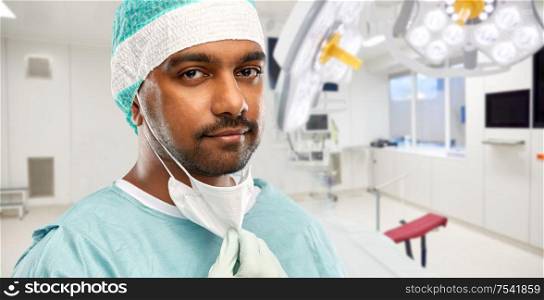 medicine, surgery and healthcare concept - close up of indian male doctor or surgeon with protective mask over operating room at hospital background. face of doctor or surgeon at hospital