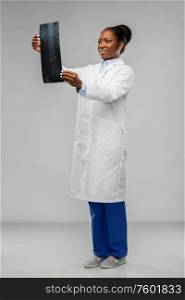 medicine, surgery and healthcare concept - happy smiling african american female doctor or surgeon in white coat looking at x-ray over grey background. african american female doctor looking at x-ray