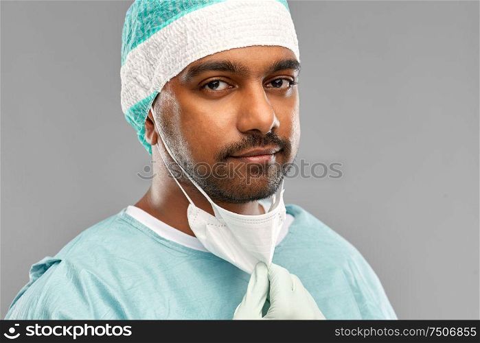 medicine, surgery and people concept - close up of indian male doctor or surgeon with protective mask over grey background. face of doctor or surgeon with protective mask