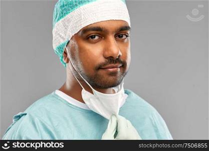 medicine, surgery and people concept - close up of indian male doctor or surgeon with protective mask over grey background. face of doctor or surgeon with protective mask