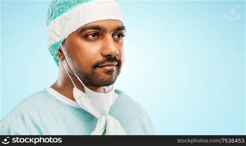 medicine, surgery and people concept - close up of indian male doctor or surgeon with protective mask over blue background. face of doctor or surgeon with protective mask
