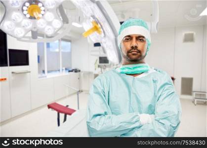 medicine, surgery and people concept - indian male doctor or surgeon in protective wear over operating room in hospital background. indian male doctor or surgeon at hospital
