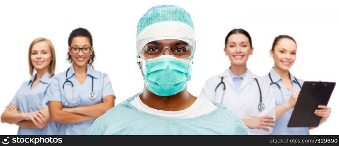 medicine, surgery and people concept - indian male doctor or surgeon in mask, goggles and protective wear over smiling healthcare workers team on white background. indian doctor or surgeon and healthcare workers