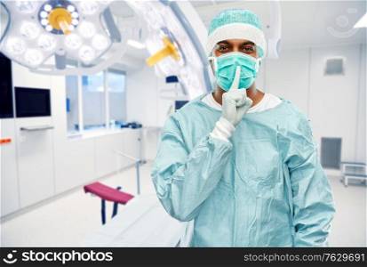 medicine, surgery and people concept - indian male doctor or surgeon in mask and protective wear over operating room at hospital background. indian male doctor or surgeon over operating room